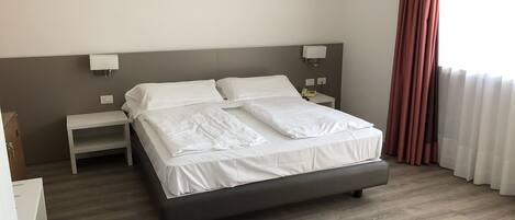 A neatly made bed with white linens, a bedside table with a lamp, and a telephone.