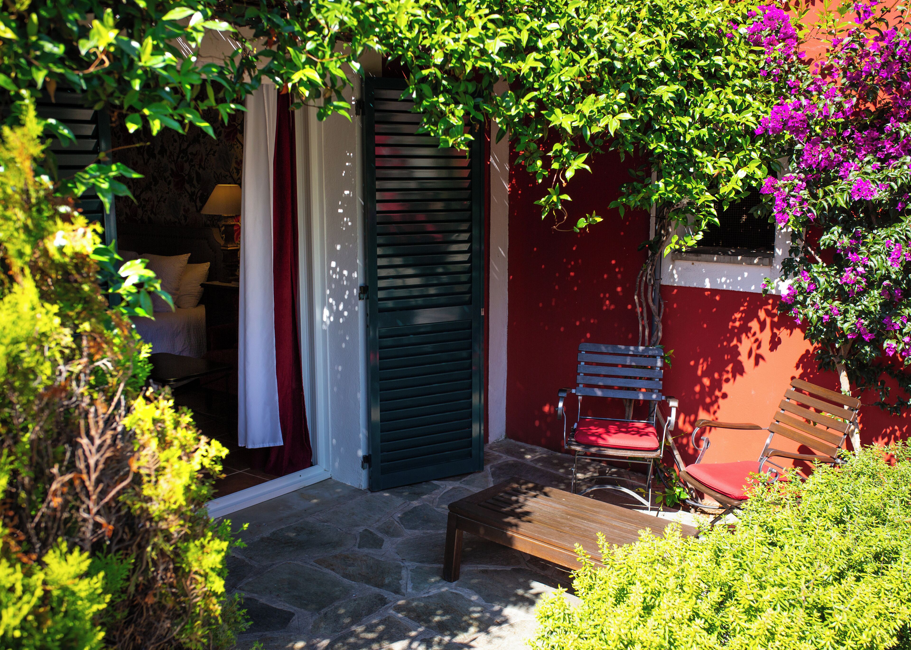 Un espace patio avec un banc en bois et une chaise, une porte avec des volets et un mur avec une fenêtre.