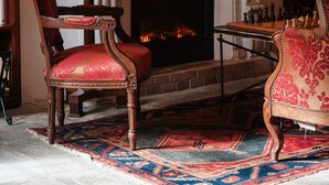 A cozy room with a fireplace, two lamps, a chessboard, and a red patterned chair.