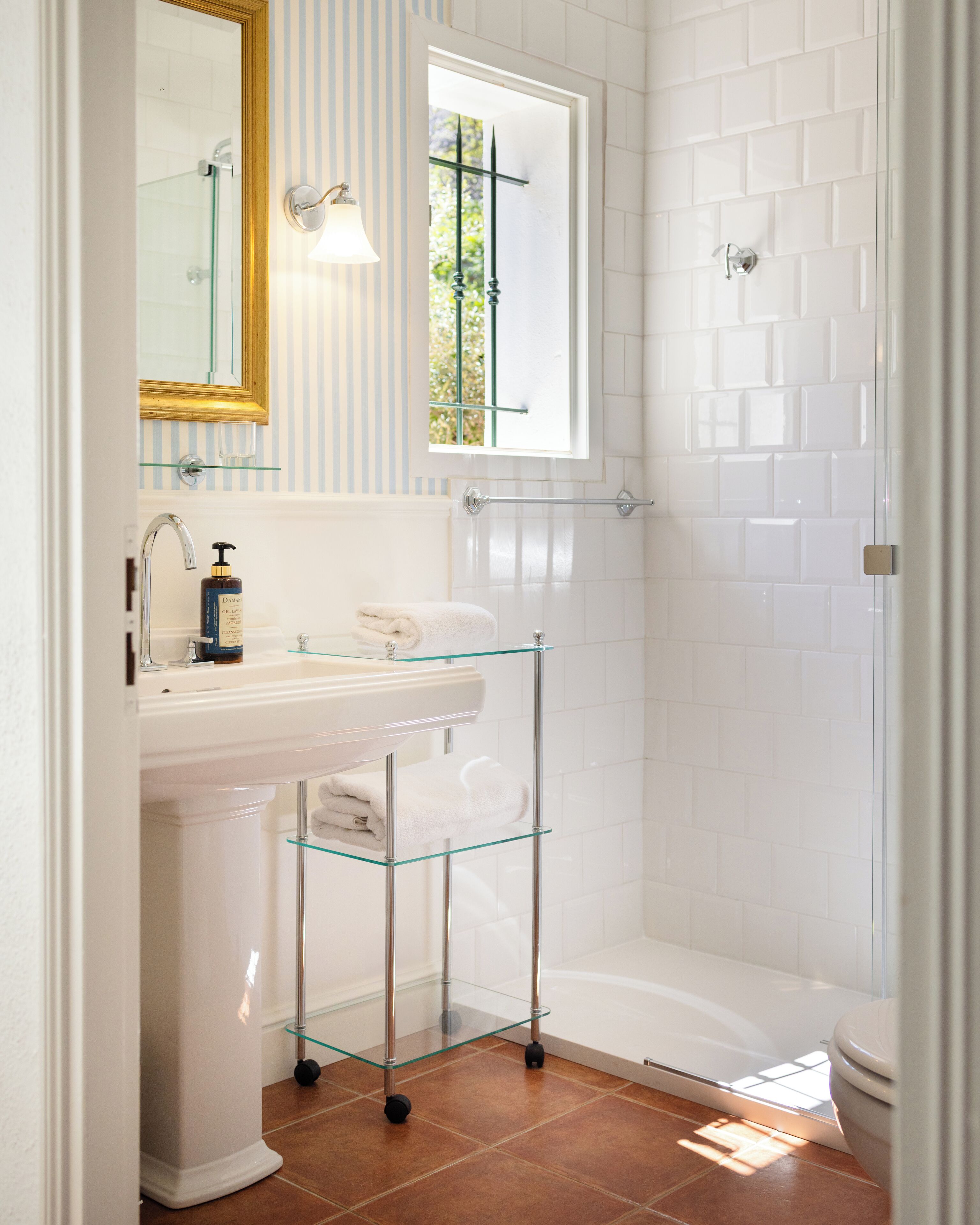 A bathroom with a white sink, a glass shelf, a towel rack, and a shower area.