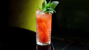 Un verre d’une boisson rouge, garnie de feuilles de menthe, posé sur une surface réfléchissante.