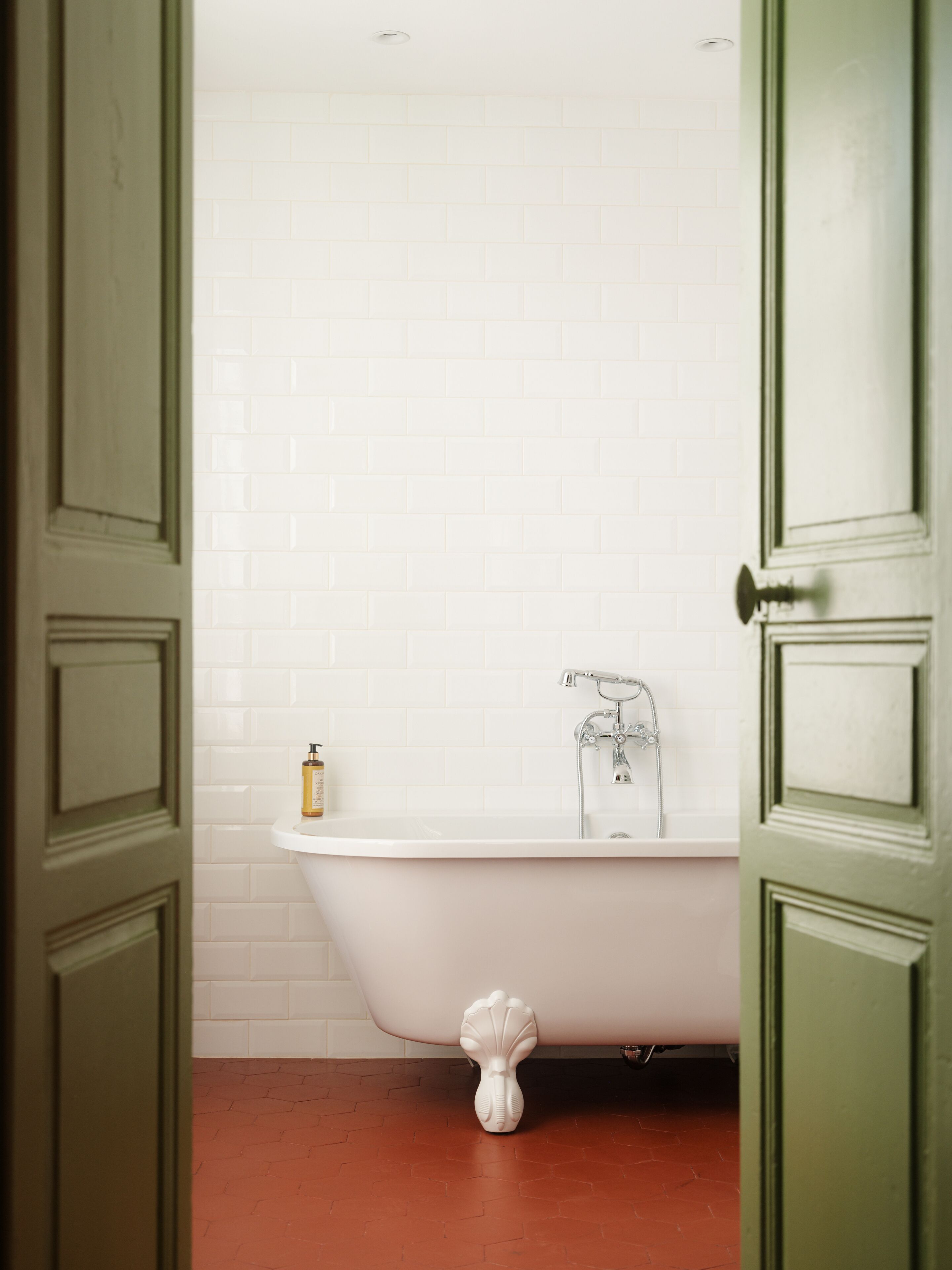 A bathroom with a white bathtub, a white tiled wall, and a green door.