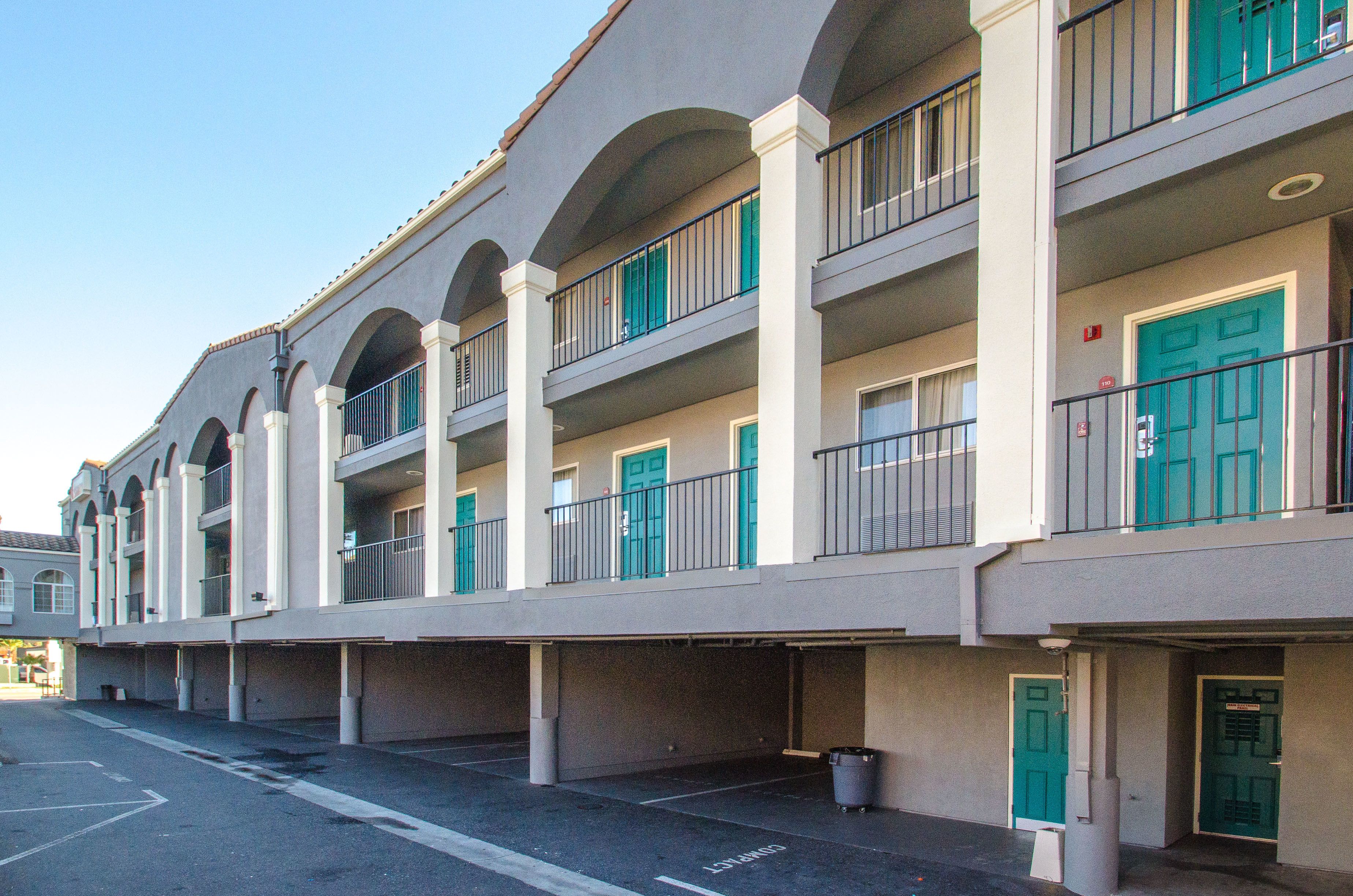 A multi-story hotel with balconies, a parking area, and a clear sky.