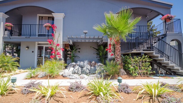 Una casa a due piani con un balcone, una scala e un giardino con diverse piante e fiori.
