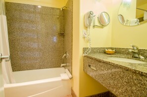 Un baño con bañera, lavabo, espejo y secador de pelo en la pared.
