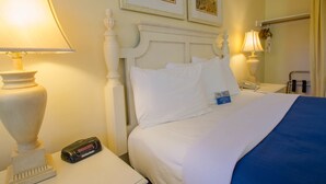 Una camera d'albergo con un letto bianco, due lampade ai lati del letto, un telefono e una sveglia digitale sul comodino.