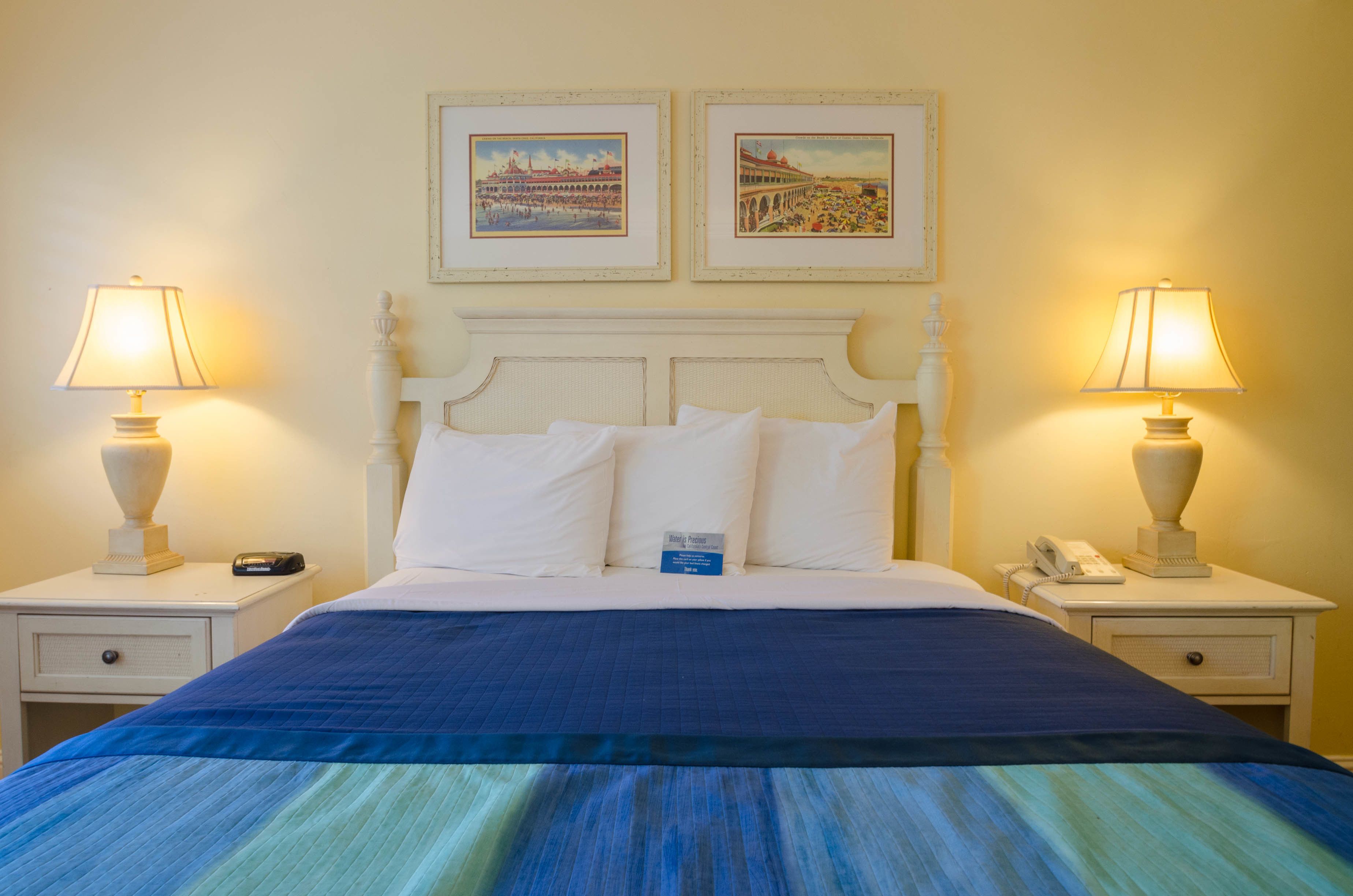 Un lit bien fait, avec du linge de lit blanc, une couvre-lit à rayures bleues et vertes, et deux tables de chevet avec des lampes et un téléphone.