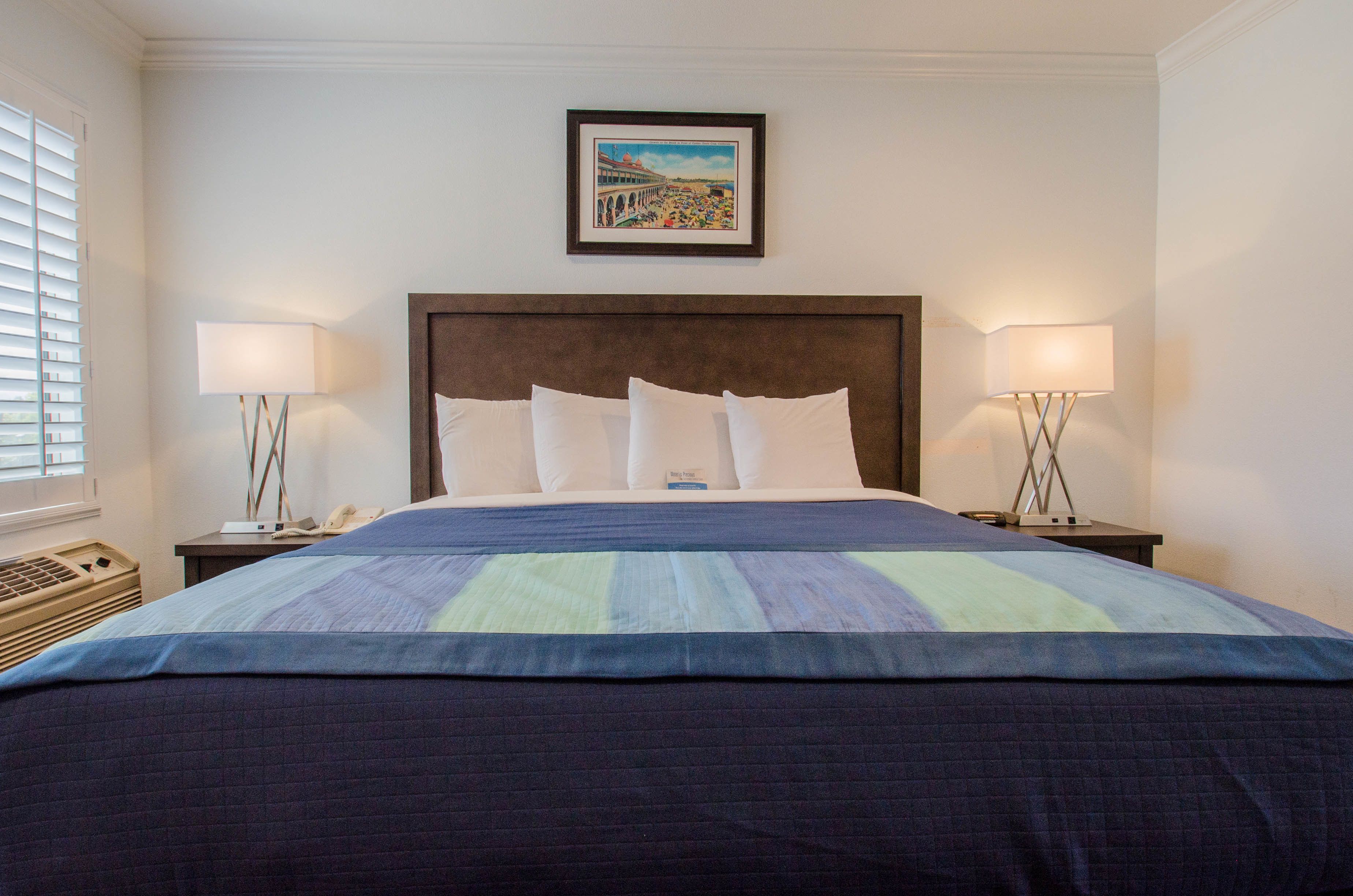 A neatly made bed with a blue and green striped bedspread, two bedside lamps, and a framed picture on the wall above the bed.