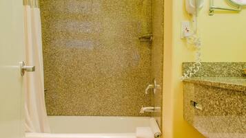 A bathroom with a bathtub, shower, and a vanity with a mirror.
