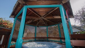Un gazebo in legno con una vasca idromassaggio sottostante, circondato da un recinto e pannelli in legno a griglia.