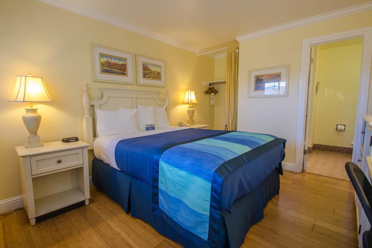 A neatly made bed with a blue and green striped bedspread, a white nightstand with a lamp, and two framed pictures on the wall.