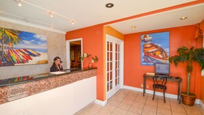 Un'area reception con un bancone, una scrivania e una sedia. Al muro, un quadro raffigura una spiaggia, una pianta in vaso e una porta che conduce in un'altra stanza.