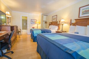 A hotel room with two beds, a desk, a chair, and a bathroom visible through an open door.