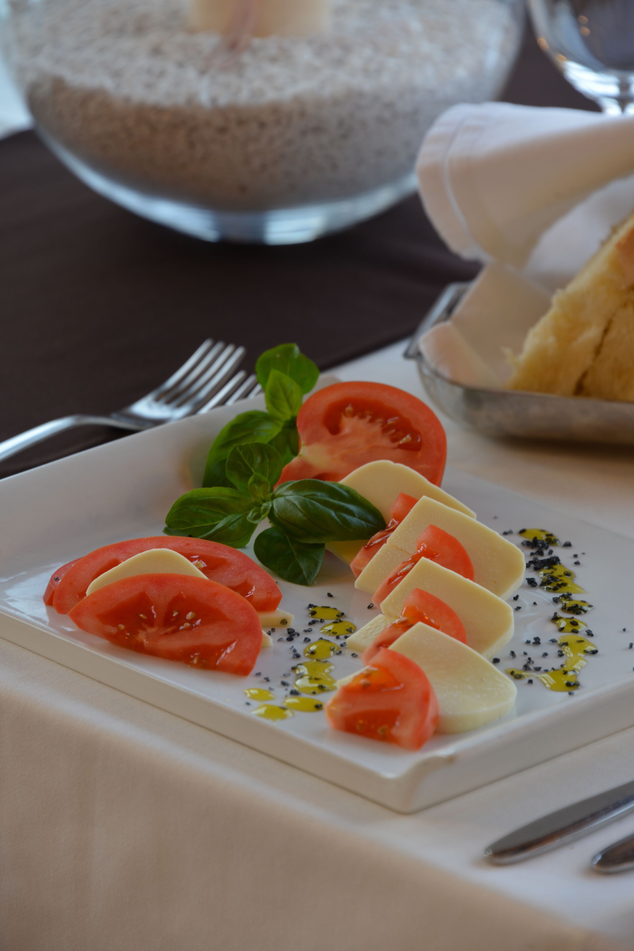 Una ensalada Caprese con tomates, mozzarella y albahaca, acompañada de un tenedor y un bol de pan.
