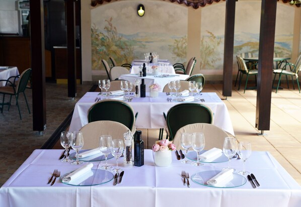Un restaurante con mesas dispuestas para comer, con manteles blancos, copas y cubiertos ordenados.