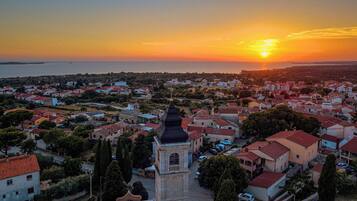 Un pueblo costero con una imponente torre de iglesia, edificios residenciales y vistas al mar al atardecer.