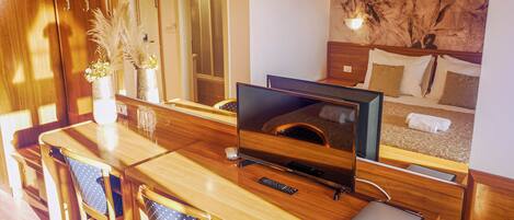 Hotelkamer met een houten bureau, een flatscreen televisie, een bed met kussens, een wandlamp en een bloemenmural.