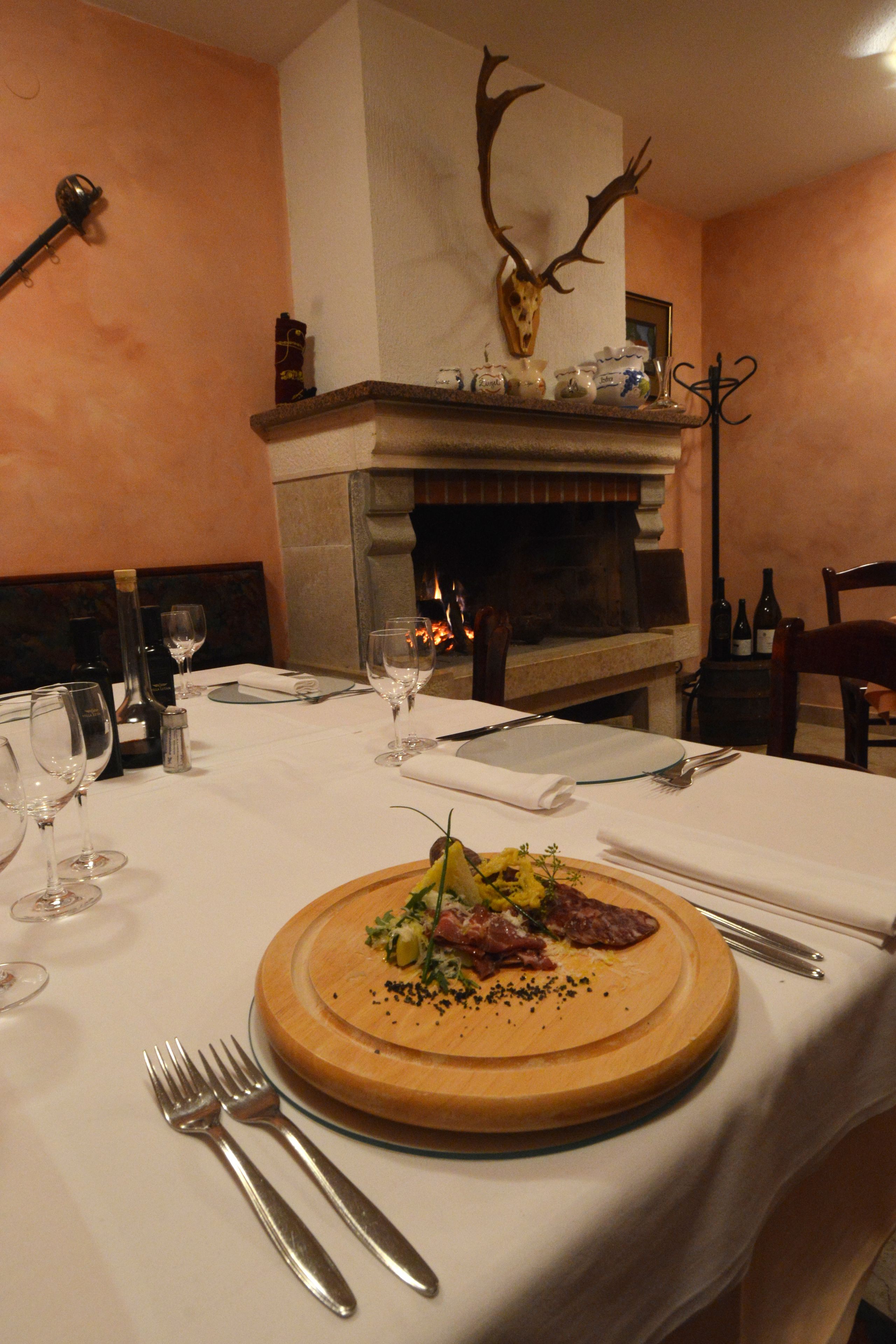 Une table à manger dressée avec des verres à vin, des couverts et une planche en bois sur laquelle est présenté un repas.
