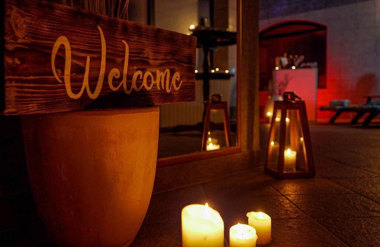 Cartell de 'Welcome' en un marc de fusta, una planta en test i tres espelmes enceses al terra.