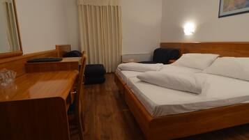 A hotel room with a wooden bed, a desk, a chair, and a window with curtains.