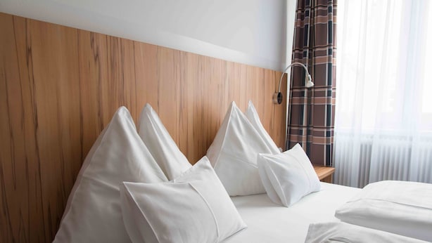 A hotel room with a wooden headboard, white bedding, and a bedside lamp. - Pension Dr. Geissler (Vienna)