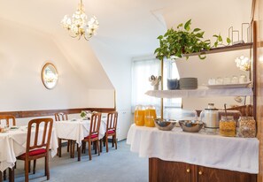 A dining area with tables set for four, a chandelier, a mirror, and shelves with jars and a plant.