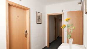 A hallway with wooden doors, a framed picture on the wall, and a vase with flowers on a table. - Pension Dr. Geissler (Vienna)