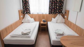 A room with two single beds, a small wooden nightstand, a round wooden table, and floral curtains.