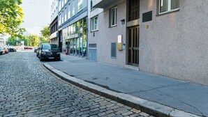 A street view with a building featuring a modern facade, a cobblestone street, and parked cars. - Pension Dr. Geissler (Vienna)