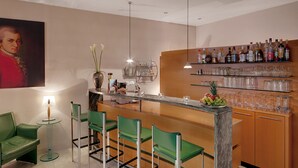 Een moderne bar met groene barstoelen, een marmeren aanrechtblad en diverse drankflessen op planken.