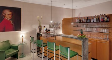 Un área de bar moderna con taburetes verdes, una encimera de mármol y una variedad de botellas de licores en estantes.