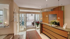 Een moderne hotellobby met een receptiebalie, een grote spiegel en uitzicht op het buitengebied door glazen deuren.