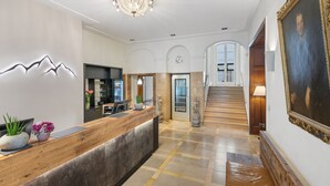 A reception area with a wooden reception desk, a wall-mounted clock, a staircase leading to an upper floor, and a large framed portrait on the wall.