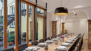 A dining area with a long table set for a meal, large windows, and a staircase leading outside.