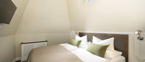 Un dormitorio con cama, mesita de noche, televisor montado en la pared, ventana y radiador.