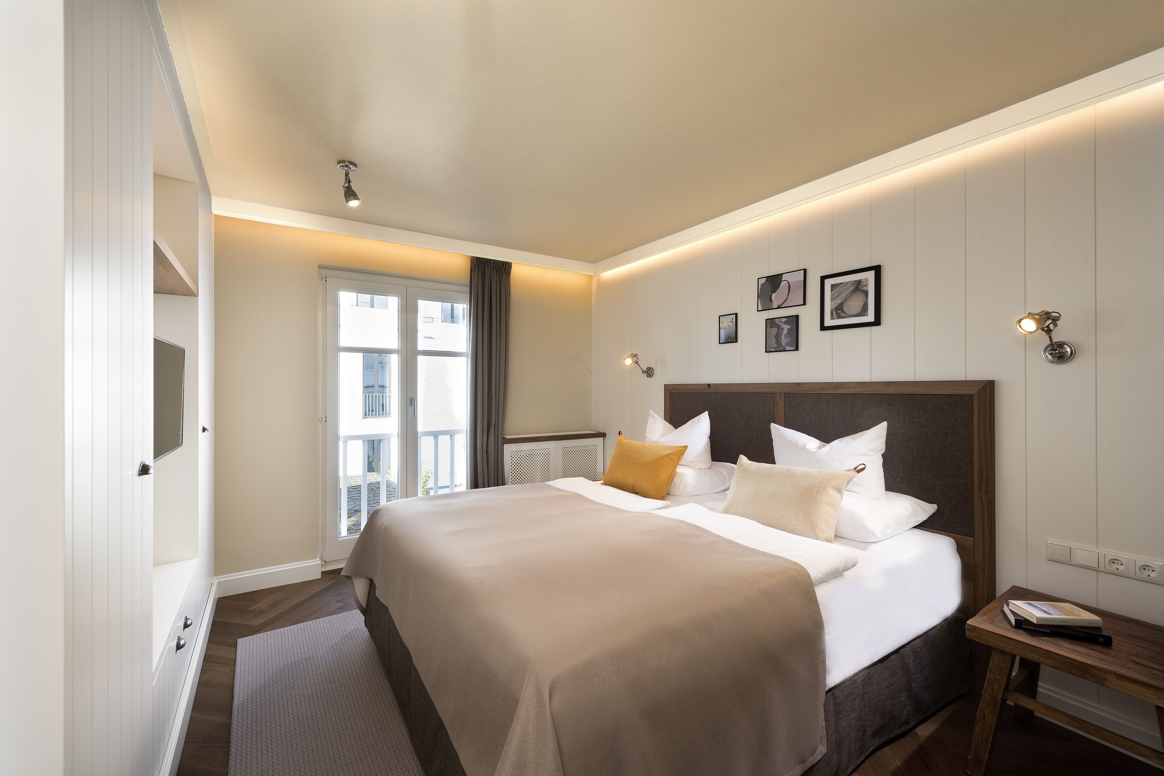 A hotel room with a large bed, a bedside table, a window with curtains, and wall-mounted artwork.