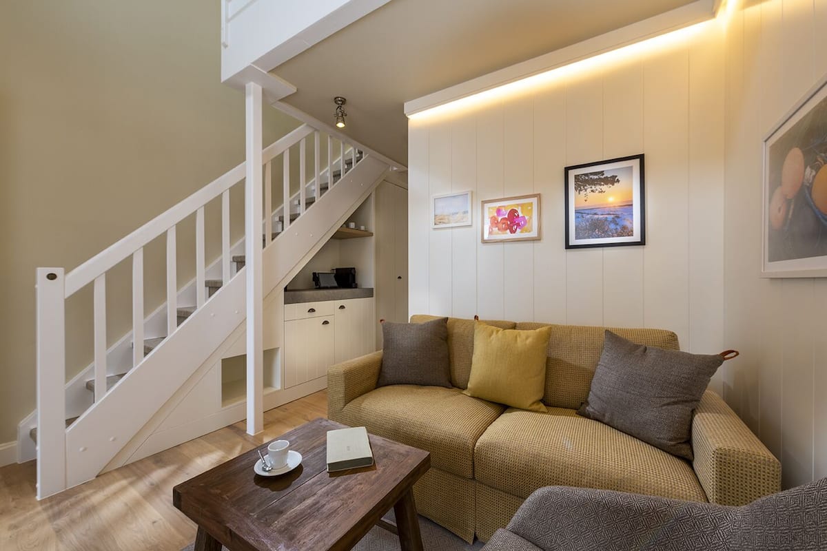 Una sala de estar con una escalera, un sofá, una mesa de centro y una zona de cocina.