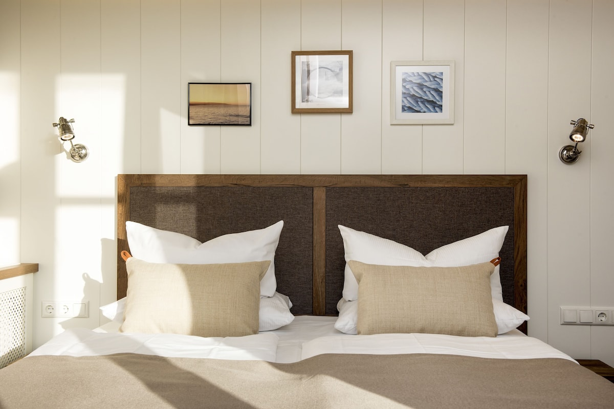 Una cama bien hecha con ropa de cama blanca y color crema, un cabecero de madera y tres obras de arte enmarcadas en la pared.