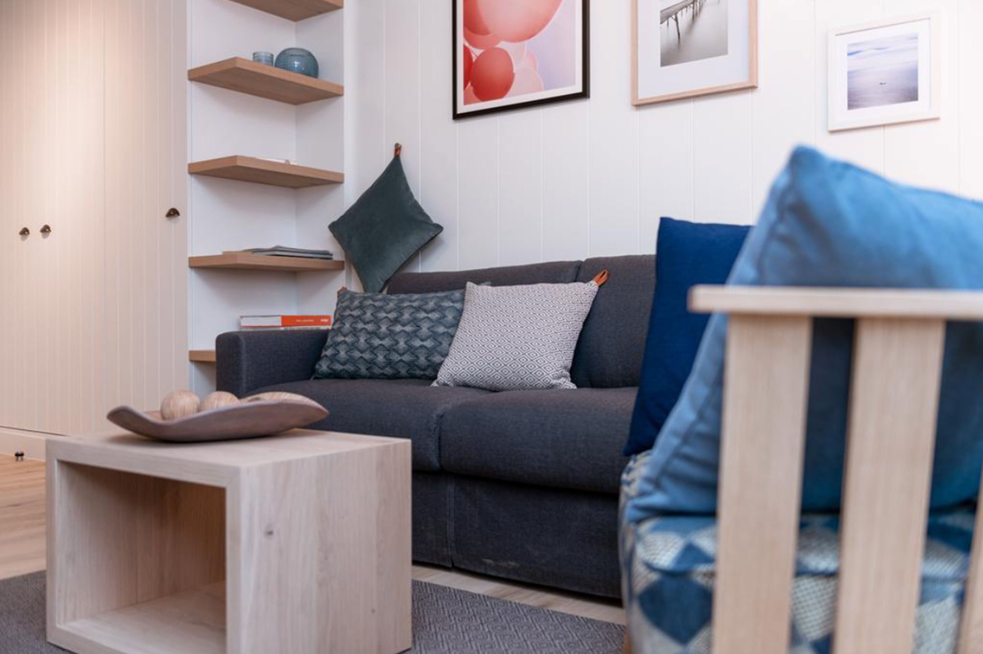 Un salon moderne avec un canapé gris, des tables d’appoint en bois et une bibliothèque.