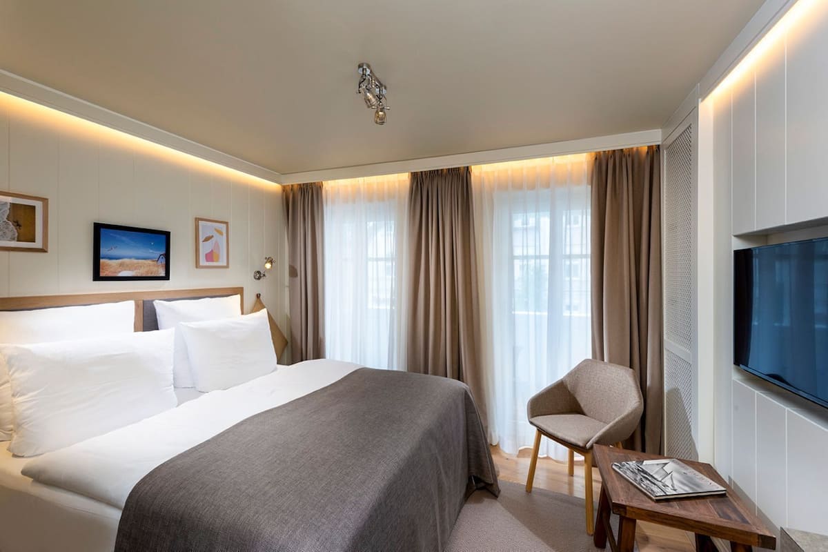 Habitación de hotel con una cama grande, una silla, un televisor y un escritorio con una revista.