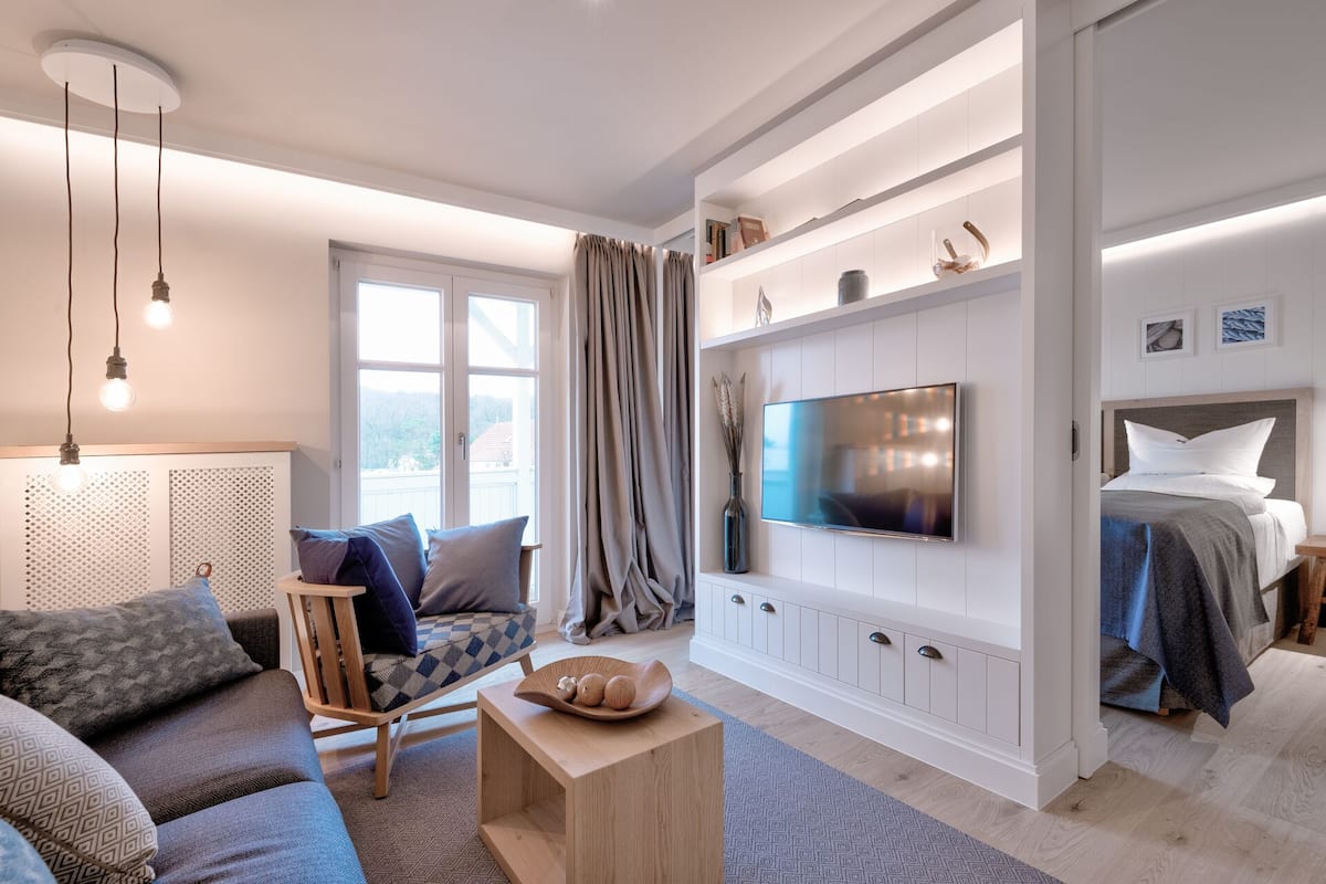 Una sala de estar moderna con sofá, una mesa de centro, televisor montado en la pared y una cama con cabecera.