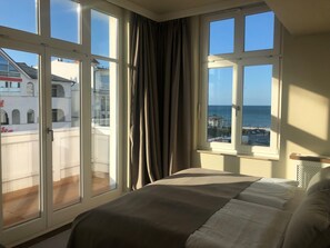 A bedroom with a large bed, a view of the sea, and a balcony with curtains. - LOEV - VELA Hotel (Binz)