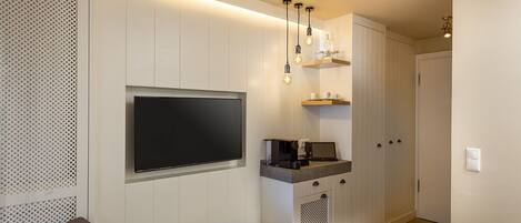 Un dormitorio moderno con una televisión de pantalla plana, una mesita con una revista, una cafetera y una cama.