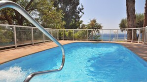 A swimming pool with a metal ladder, surrounded by a wooden deck and a glass fence. - Hotel GHT Xaloc (Castell-Platja d'Aro)