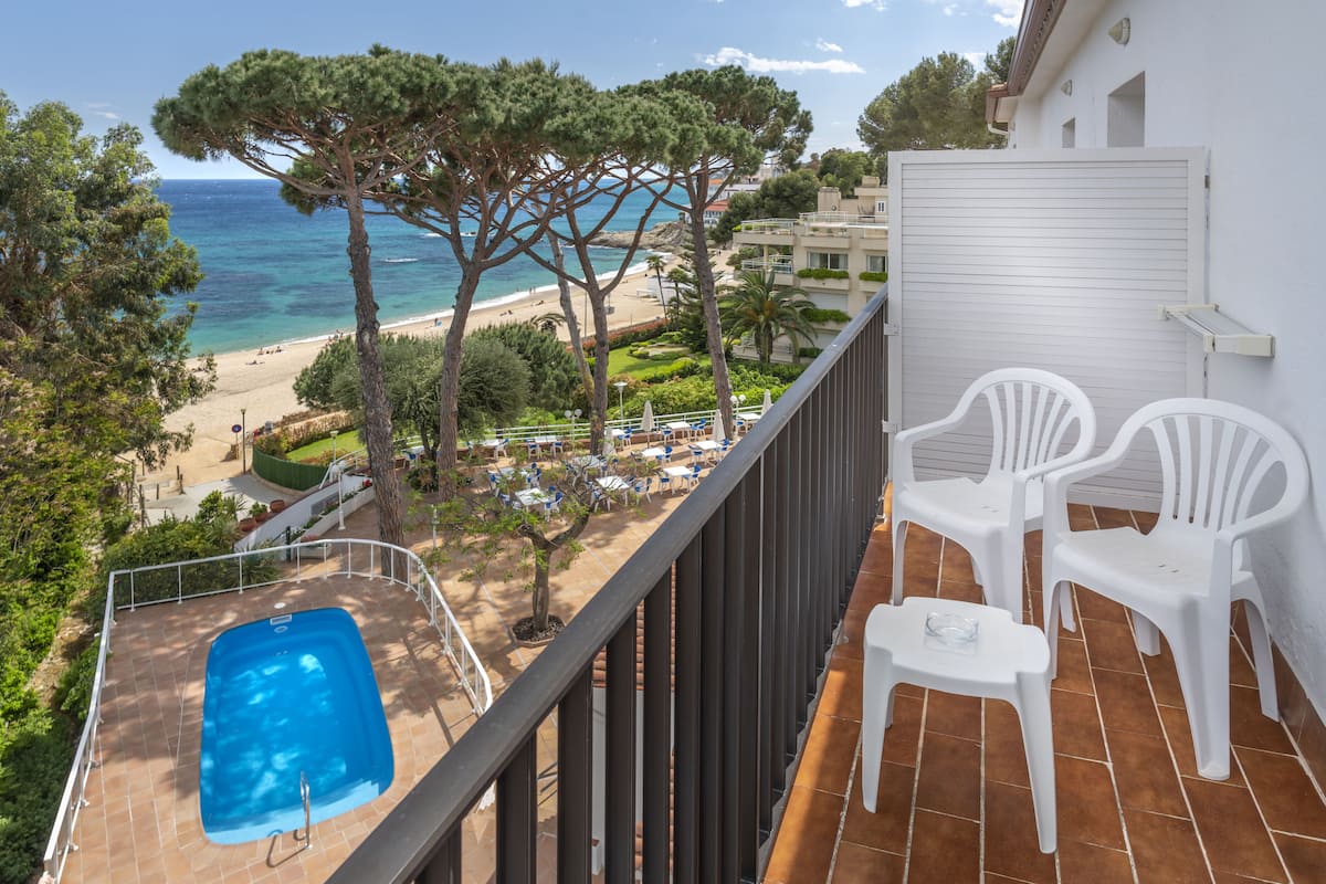 A balcony with a pool, white chairs, and a view of the beach and ocean.