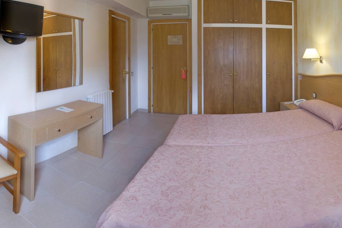 A hotel room with a bed, a desk, a chair, a wardrobe, and a TV.