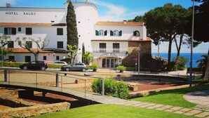 A hotel named 'HOTEL XALOC' with a white facade and red-tiled roof, situated by a coastal road with a clear view of the sea. - Hotel GHT Xaloc (Castell-Platja d'Aro)