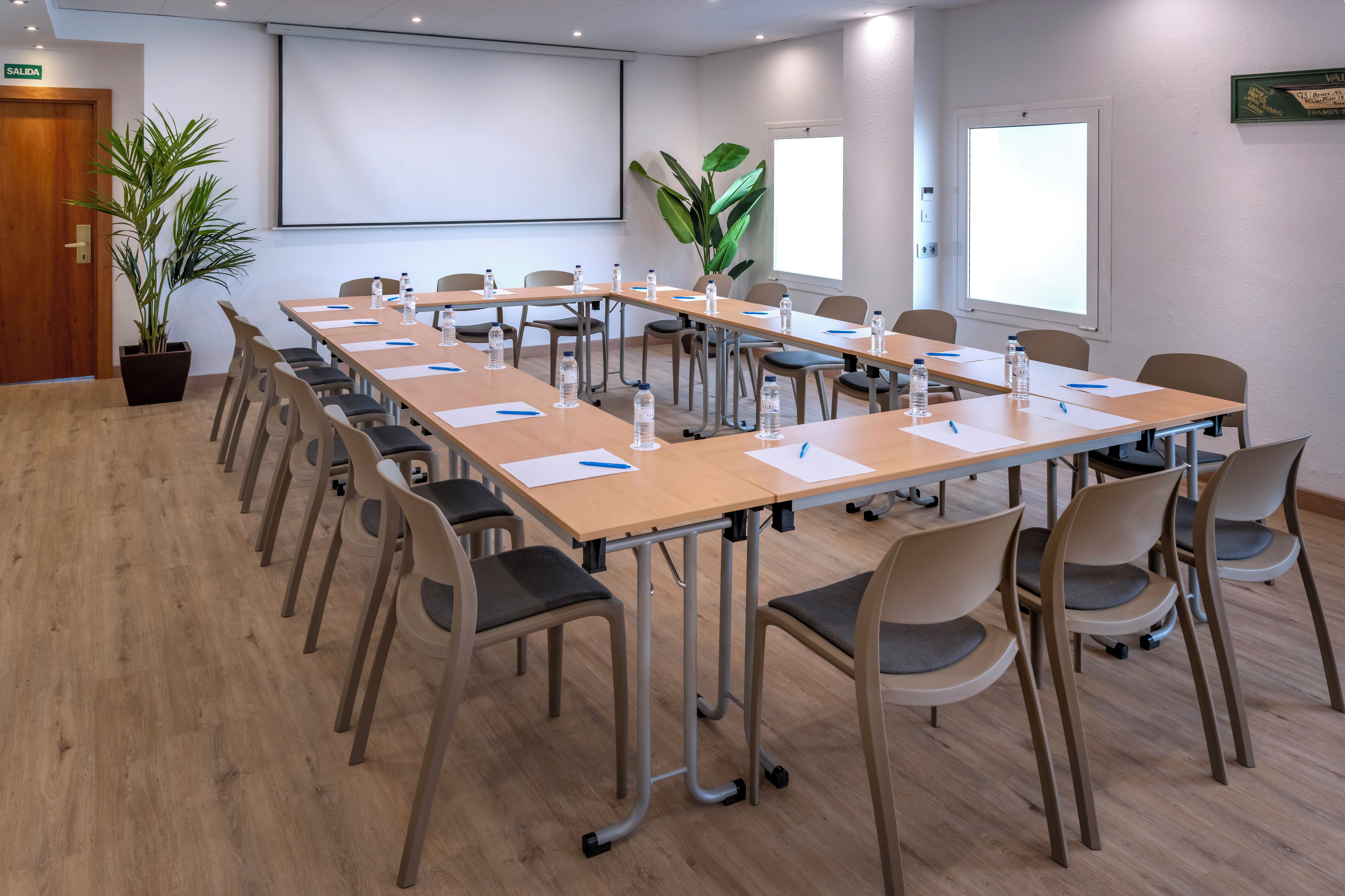 A conference room with a long table, chairs, water bottles, and a projector screen.