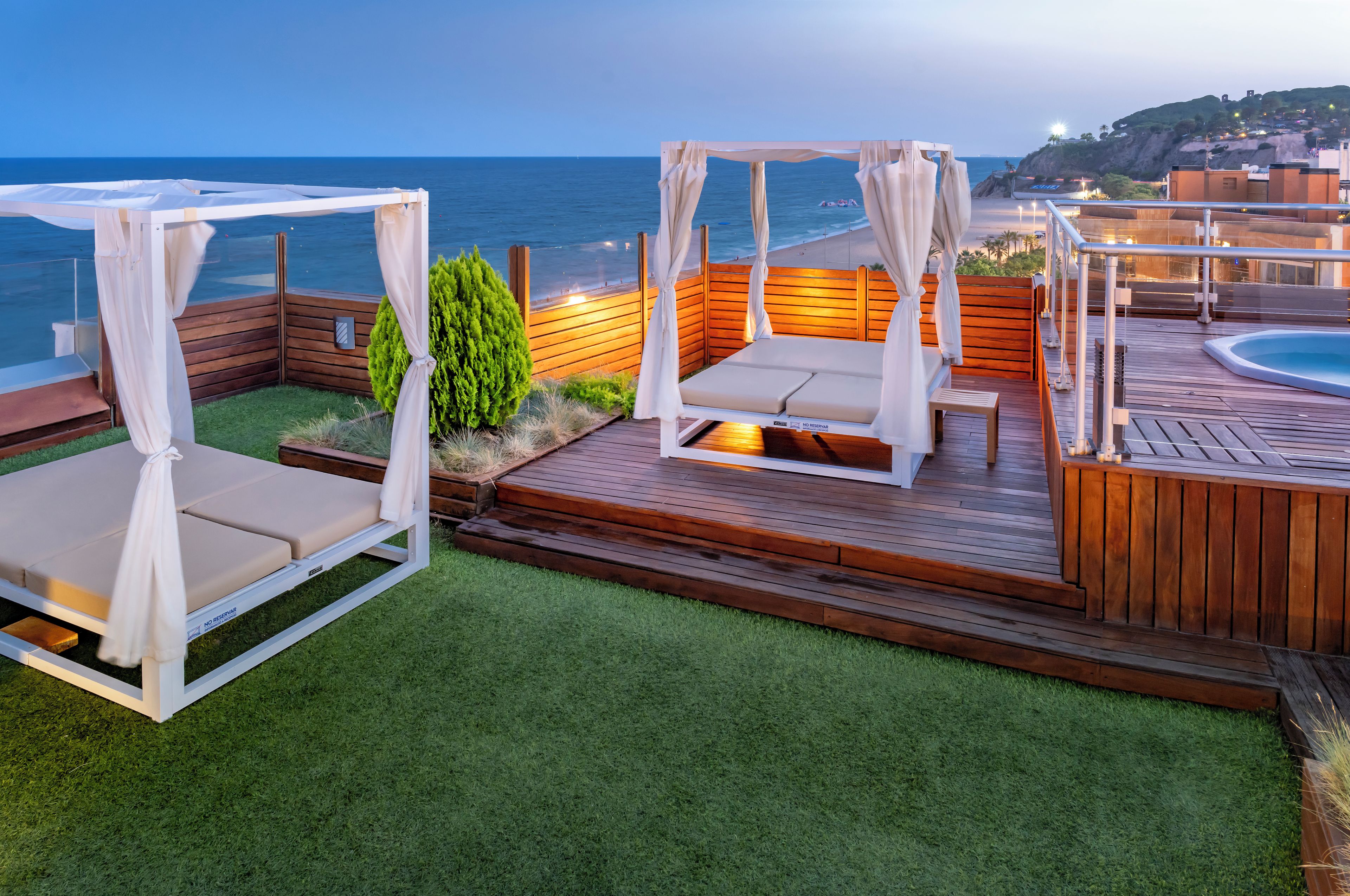 A wooden deck with two white canopy beds and a pool.