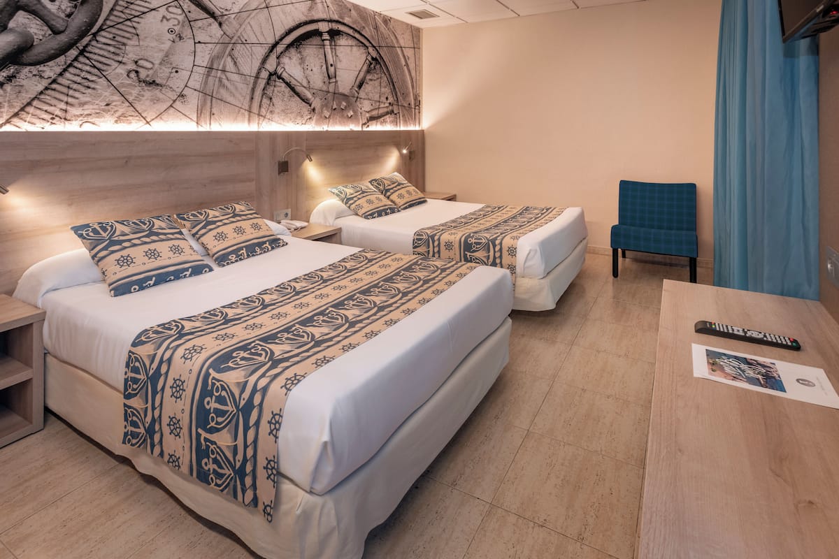 A hotel room with two beds, a wooden headboard, a blue chair, and a remote control on a table.